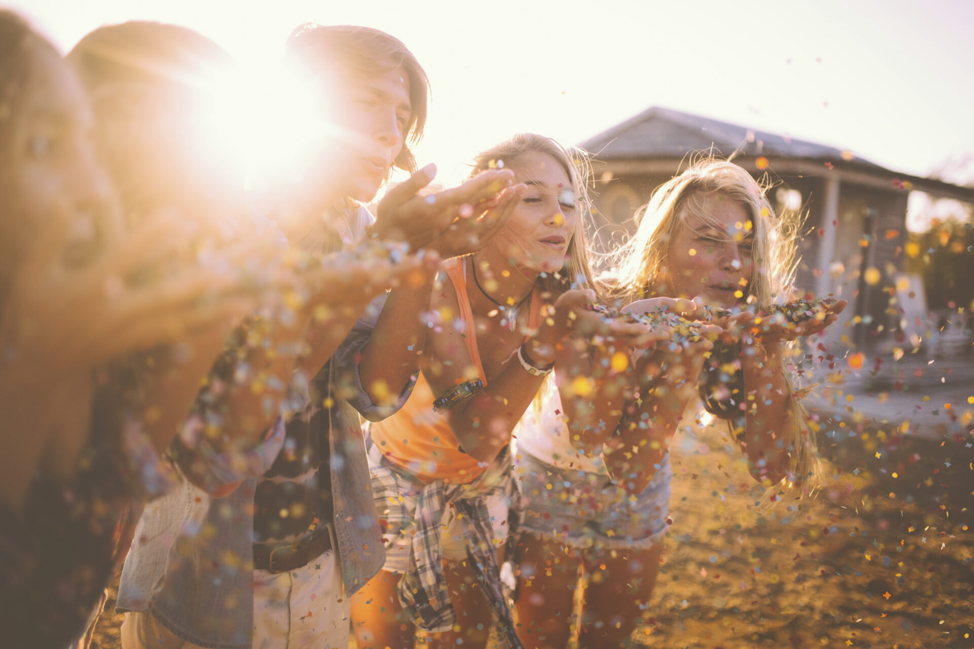 Teens blowing colourful confetti together outdoors with sun flare